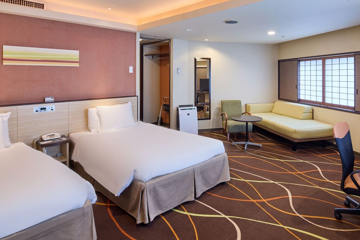 A hotel room with two beds, a sofa, a small table, a TV, and a tray with water bottles.