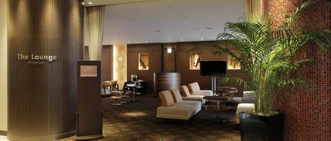 A hotel lobby with a reception desk, seating area, and a large potted plant.