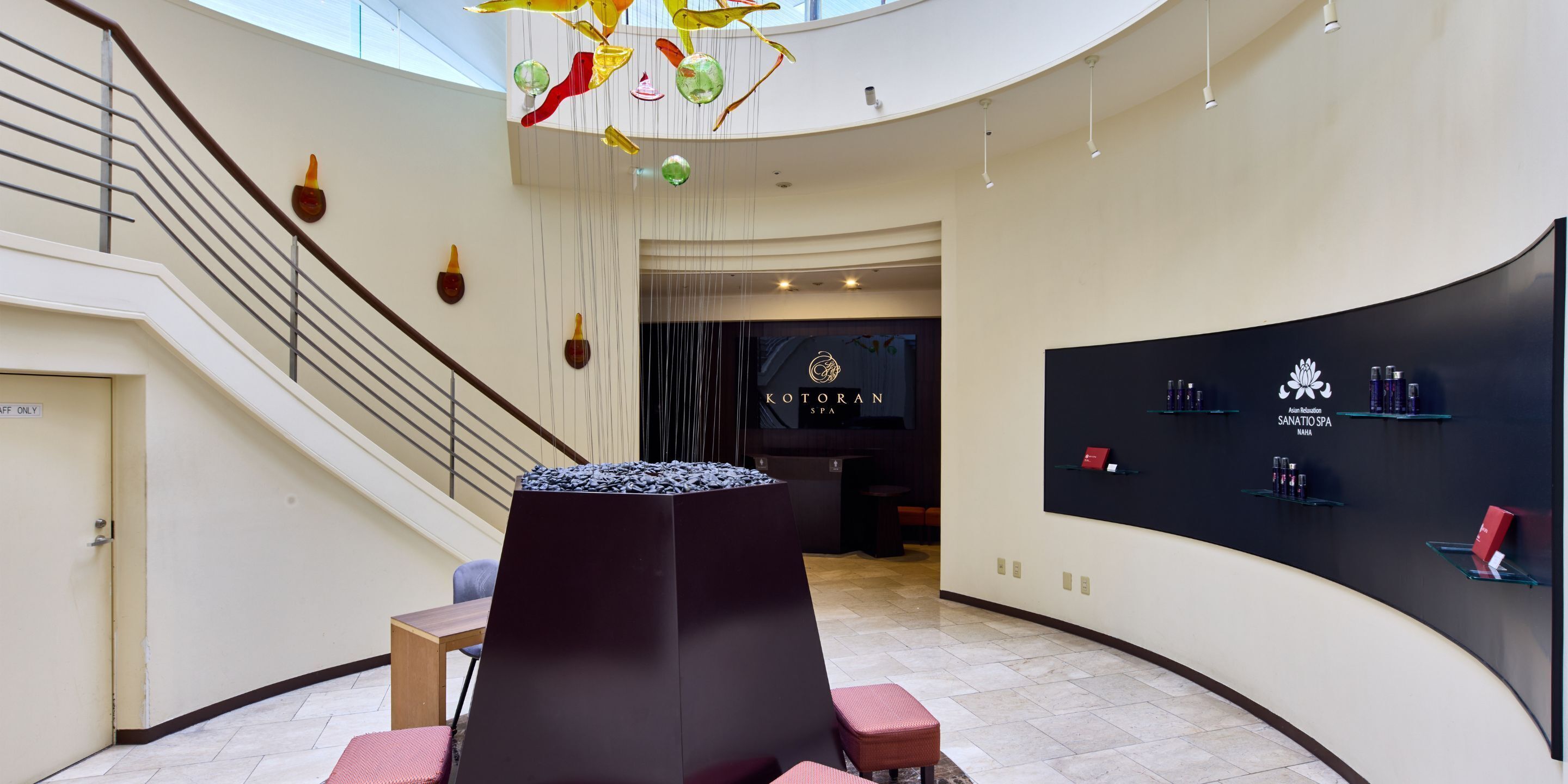 A modern interior with a reception desk, a staircase, and a wall displaying spa products.