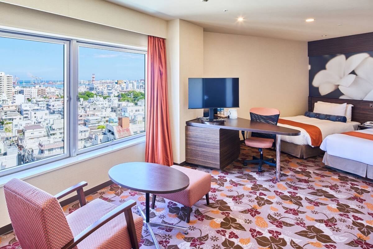 A hotel room with a large window, a desk, a bed, and a chair.