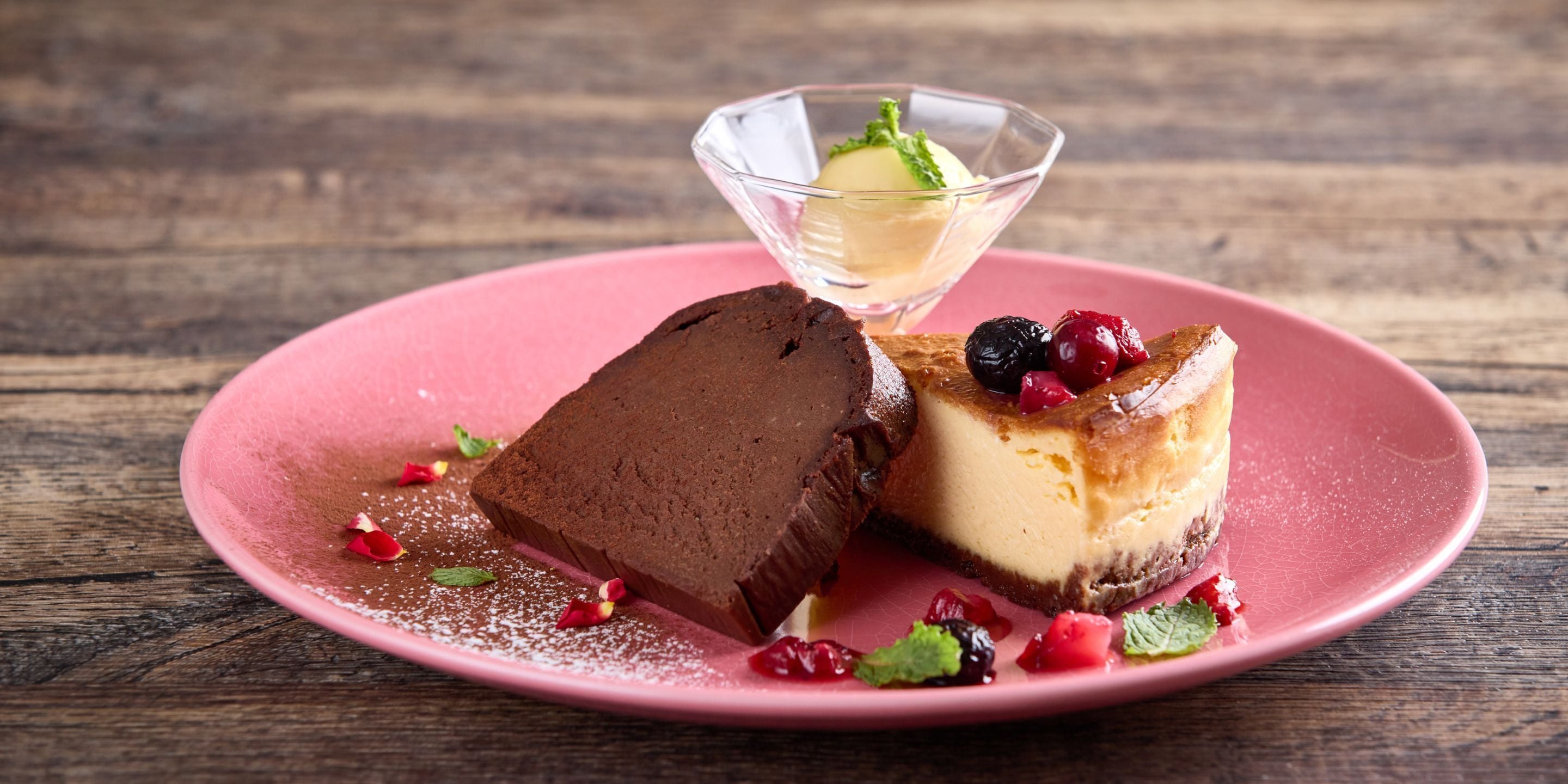 Une assiette de dessert avec un gâteau au chocolat et un gâteau au fromage, décorée de fruits rouges et de feuilles de menthe.