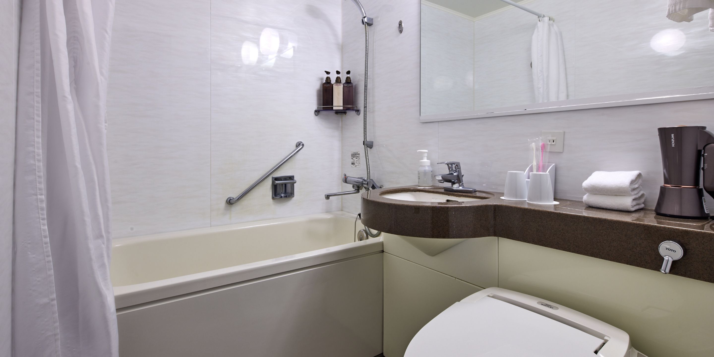 A modern bathroom with a bathtub, a sink, and a toilet. There is a showerhead, a handrail, and a towel rack.