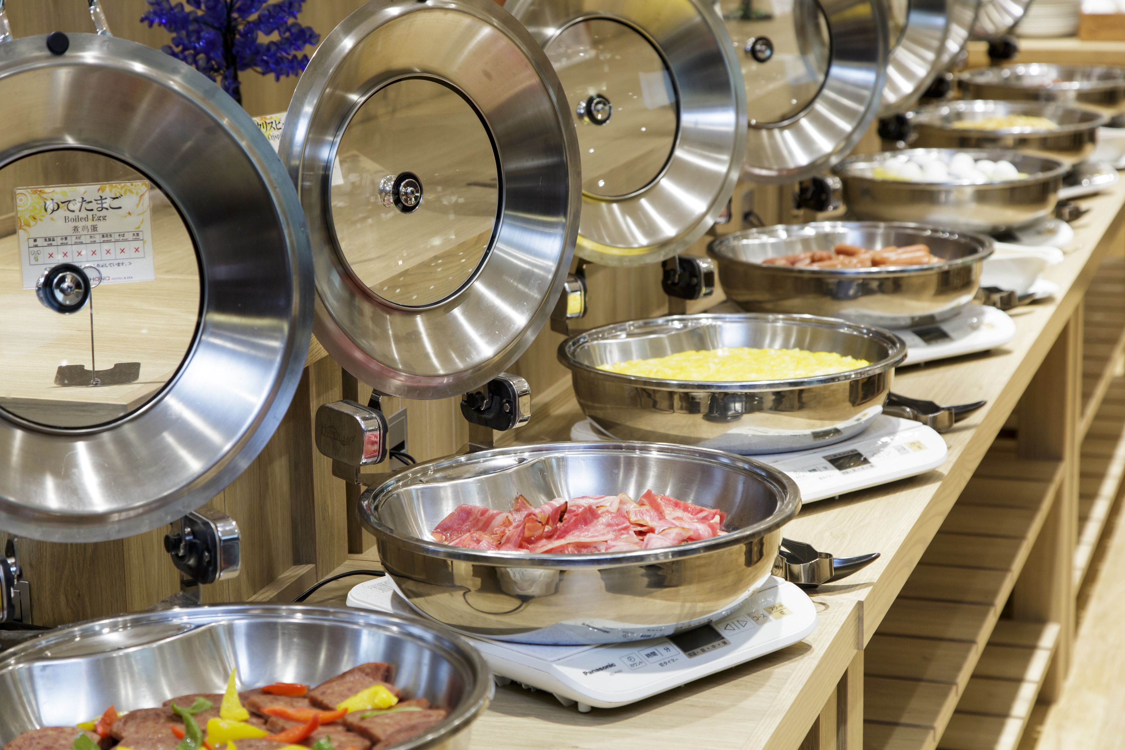 Een buffet met diverse gerechten in roestvrijstalen schalen, waaronder vlees en eieren.