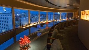Een hoog gebouwde bar met een panoramisch stadsgezicht, met een lange toonbank met flessen en decoratieve verlichting.