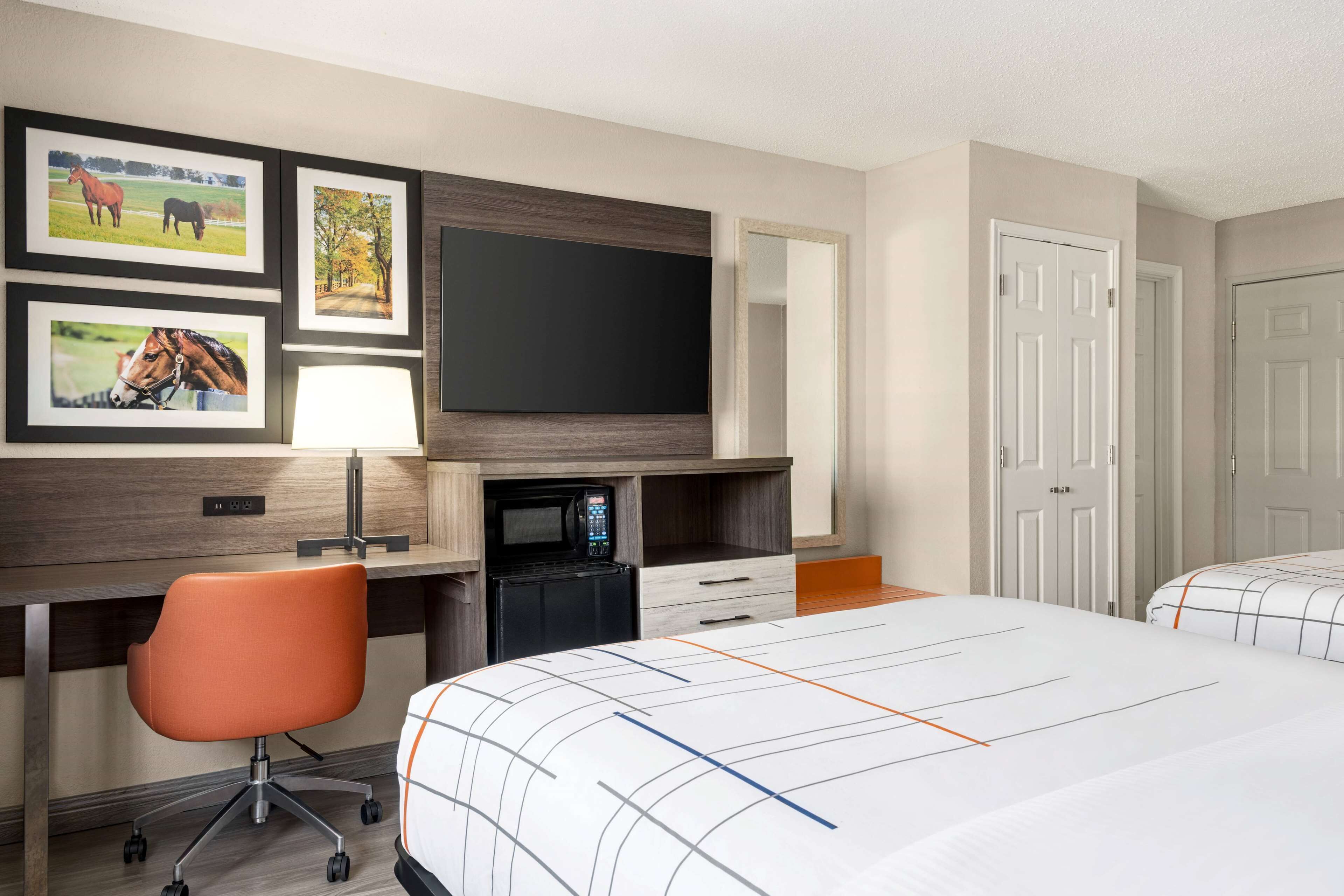 Een hotelkamer met een bed, een bureau met een computer, een magnetron, een stoel en een aan de muur bevestigde televisie.