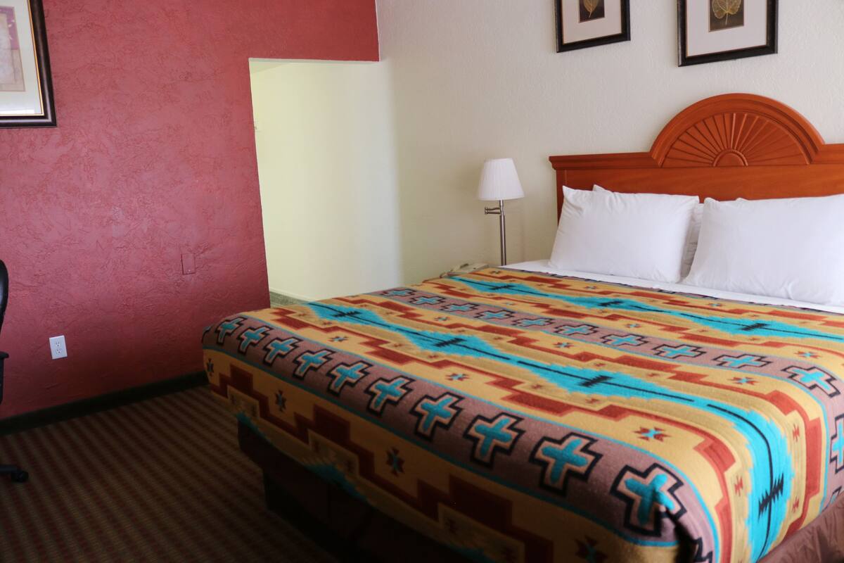 Une chambre d’hôtel avec un lit, une table de chevet, une lampe et un mur orné de tableaux.