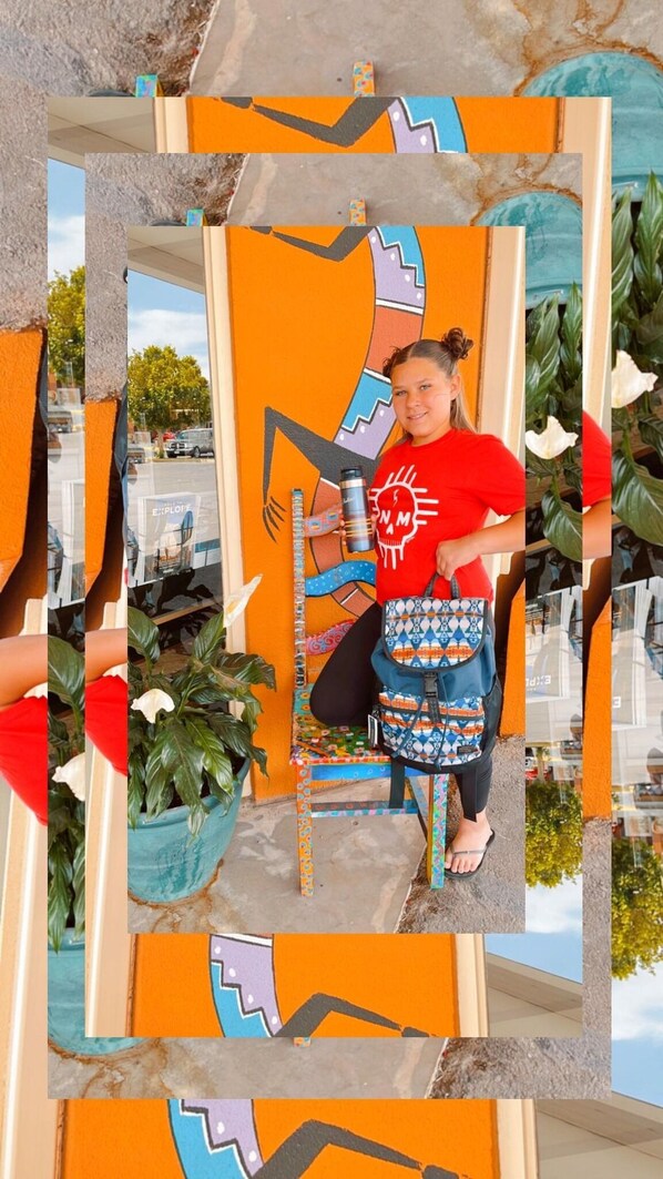 A person sitting on a chair with a colorful bag, in front of a wall with a geometric pattern.