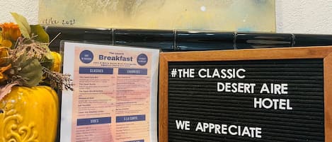 Un panneau affichant le menu du petit-déjeuner à l’hôtel The Classic Desert Aire, proposant une variété de plats classiques et appréciés, ainsi qu’un code QR pour obtenir de plus amples informations.