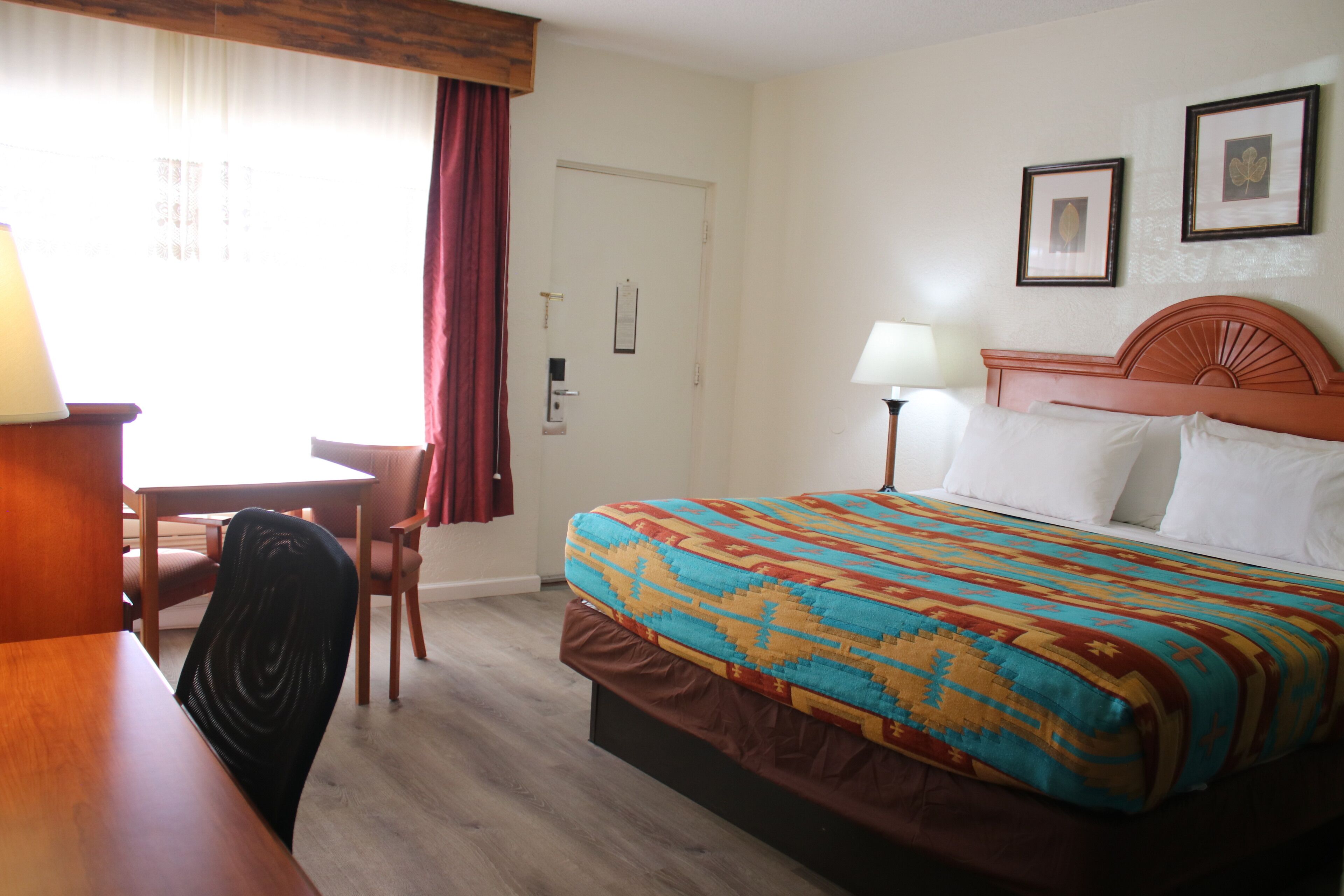 A hotel room with a bed, a desk, a chair, and a lamp.