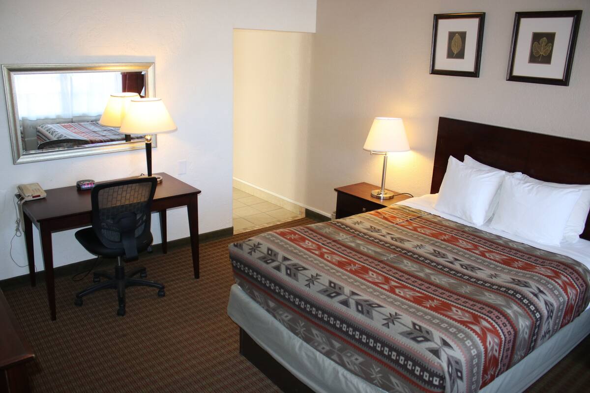 Une chambre d’hôtel comprenant un lit, deux tables de chevet avec des lampes, un bureau avec une chaise, un téléphone et un miroir.