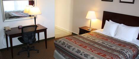 A hotel room with a bed, two bedside tables with lamps, a desk with a chair, a telephone, and a mirror.