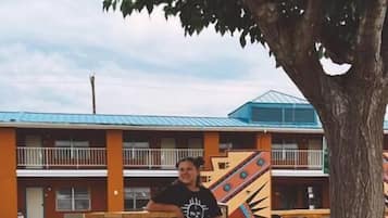 A person sitting on a wooden bench under a tree, with a building in the background.
