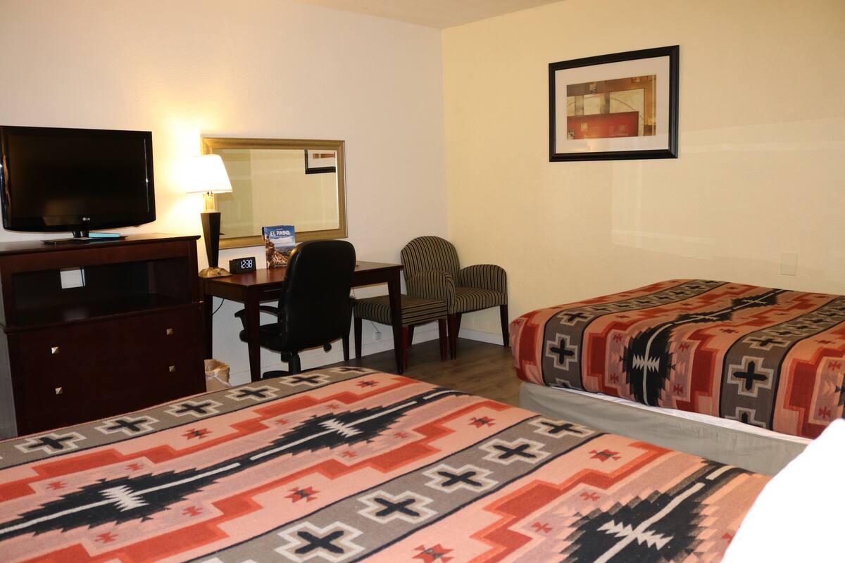 Une chambre d’hôtel équipée d’une télévision, d’un bureau, de deux chaises et de deux lits avec des couvertures à motifs.