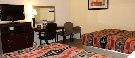 Une chambre d’hôtel équipée d’une télévision, d’un bureau, de deux chaises et de deux lits avec des couvertures à motifs.