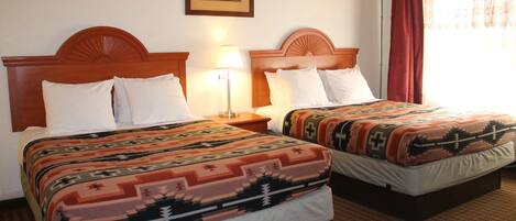 A hotel room with two beds, each with a patterned bedspread and white pillows. There is a framed picture on the wall above the beds and a floor lamp between them.