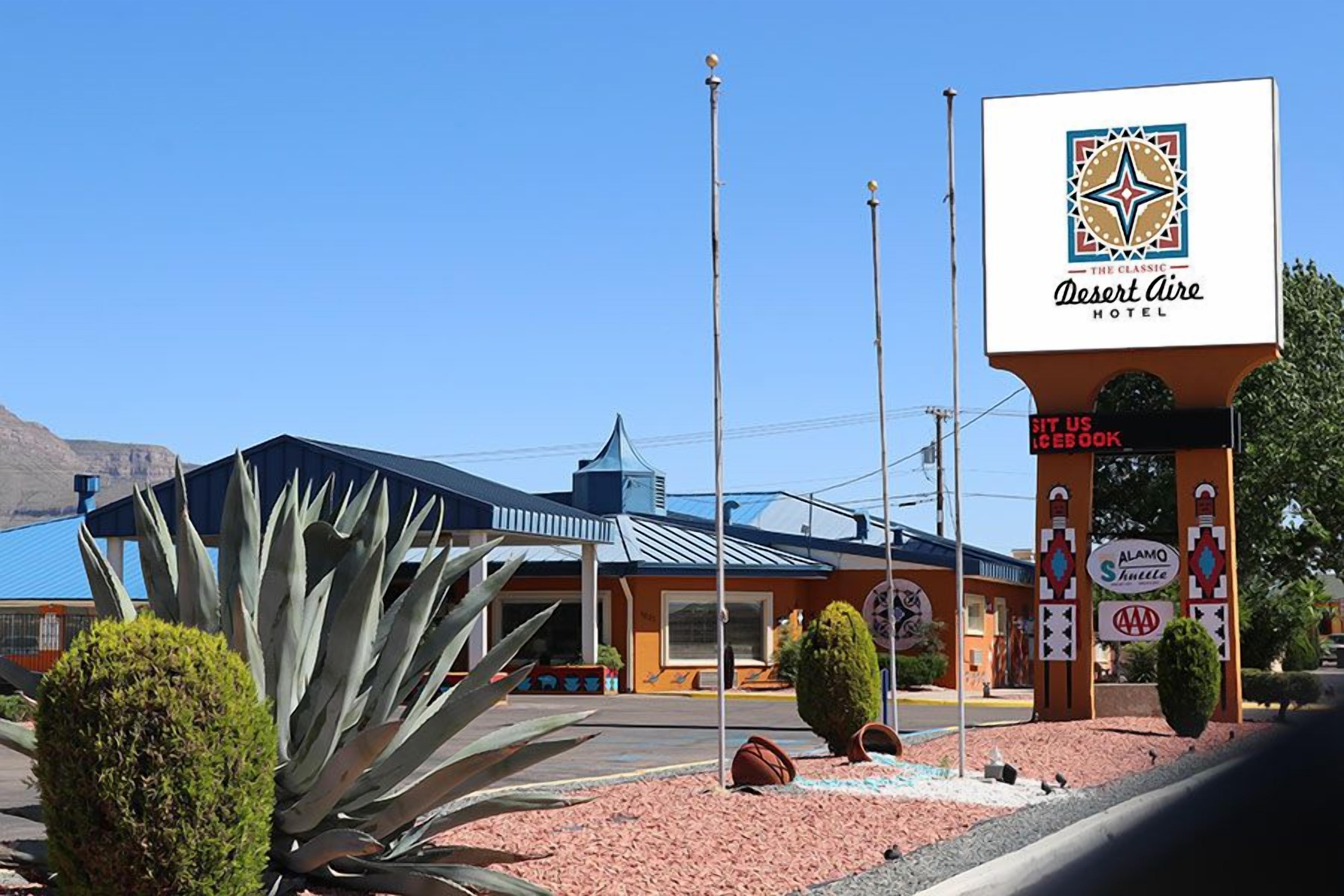 Un hôtel Desert Aire, reconnaissable à son enseigne bien visible, à son bâtiment bleu doté d’un toit en pente et à un grand agave placé au premier plan.