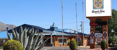 A Desert Aire Hotel with a prominent sign, a blue building with a sloped roof, and a large agave plant in the foreground.