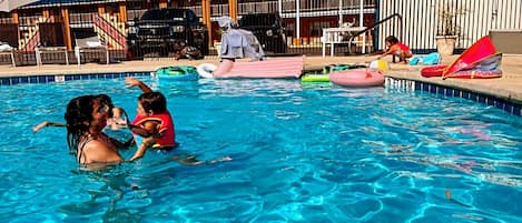 A swimming pool with inflatable toys and a covered area with chairs.