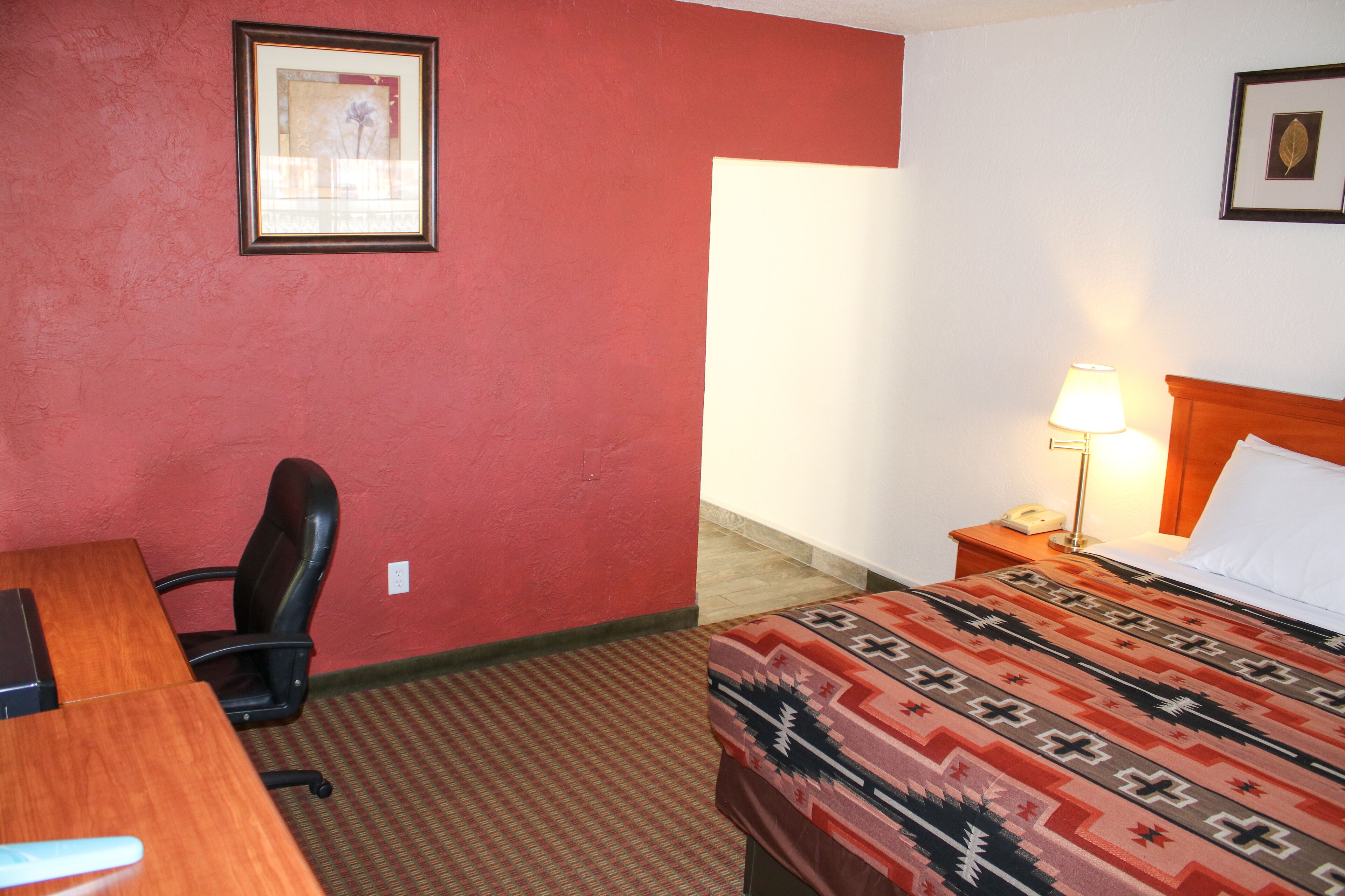 A hotel room with a bed, a desk, a chair, a lamp, and a framed picture on the wall.