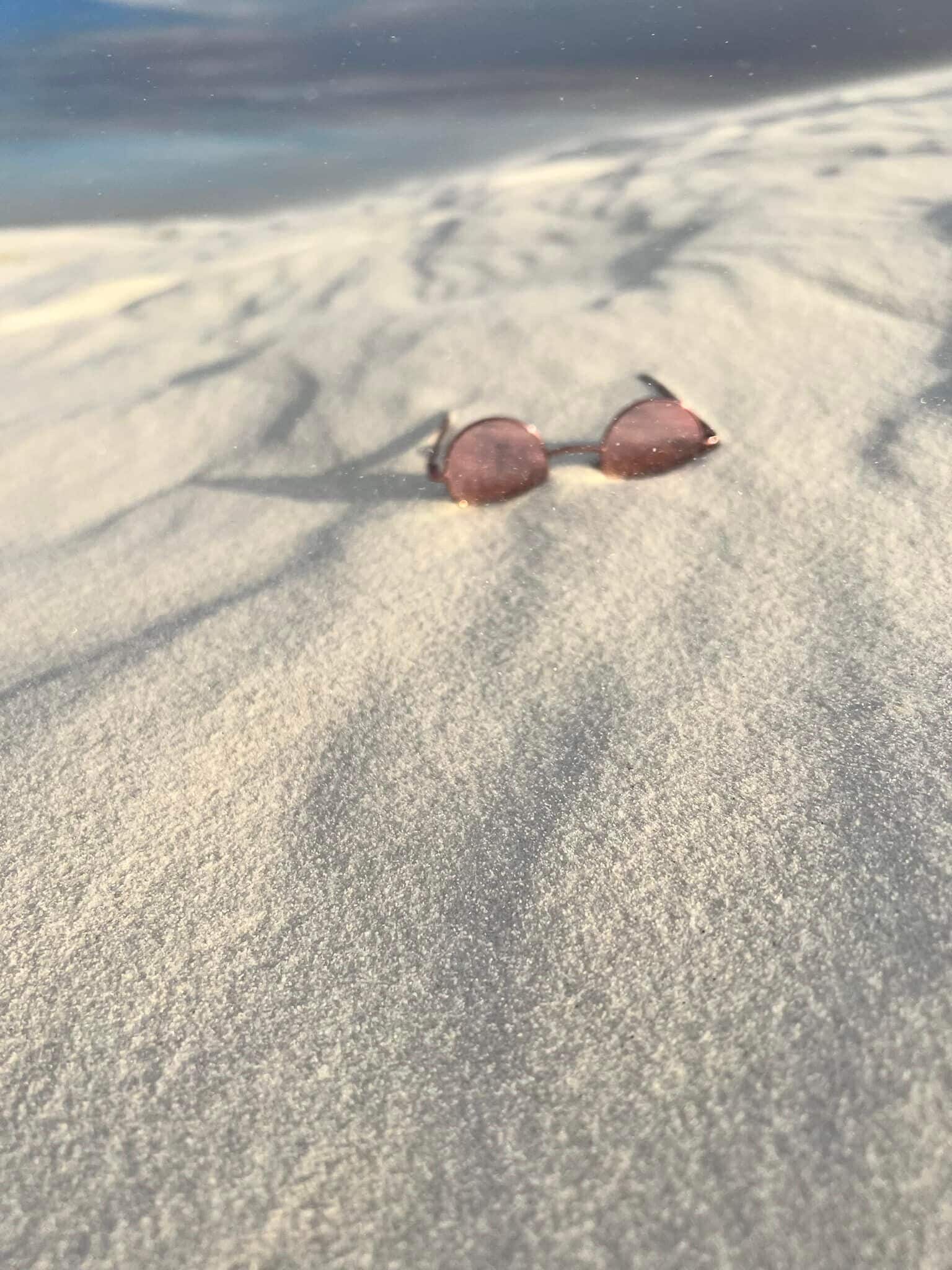 A pair of sunglasses on a sandy surface.