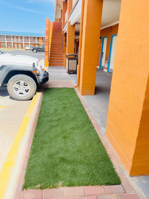 Un estacionamiento con un camino de césped artificial verde que lleva a un edificio de paredes naranja y puertas azules.