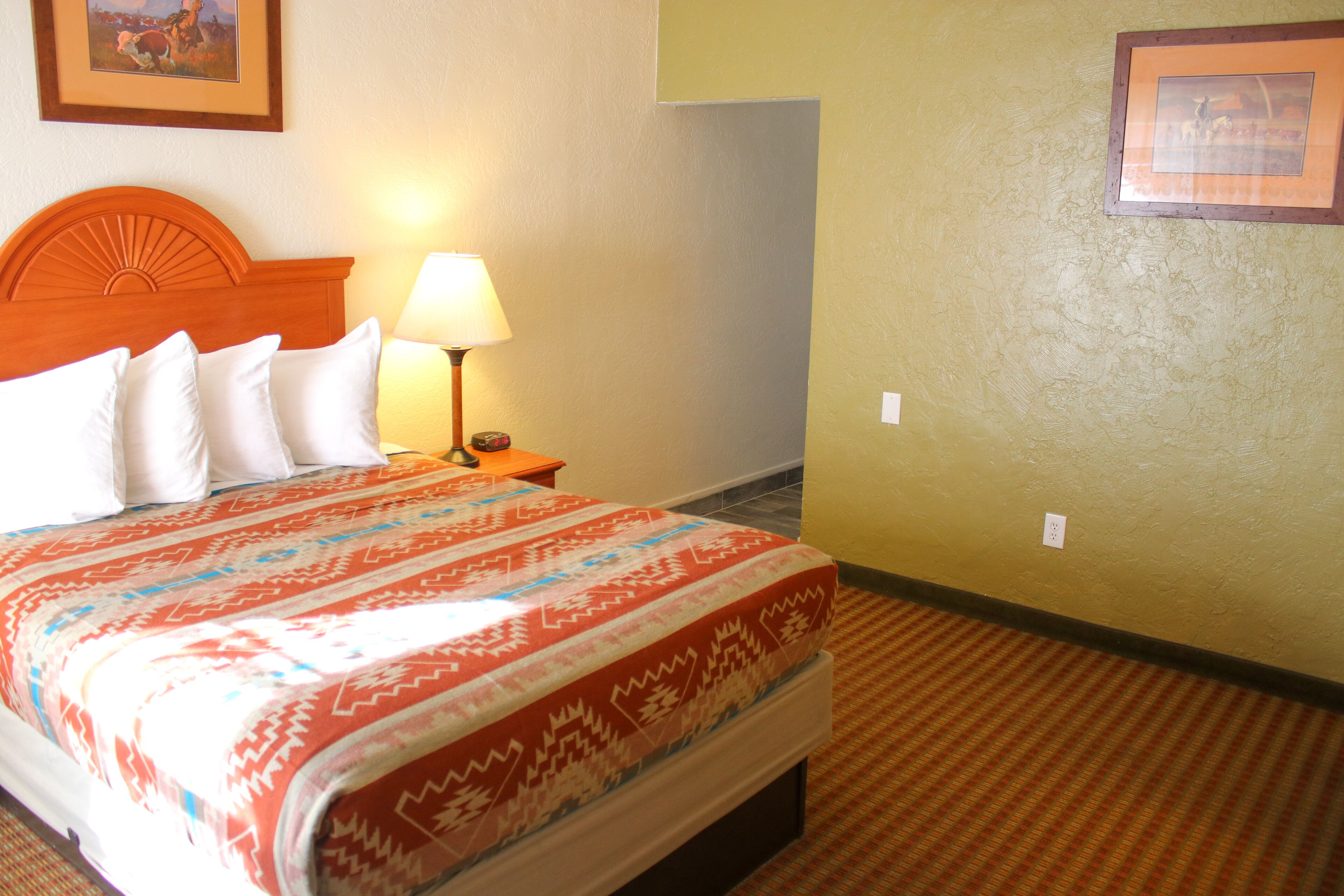 Habitación de hotel con cama, mesita de noche, lámpara y un cuadro en la pared.