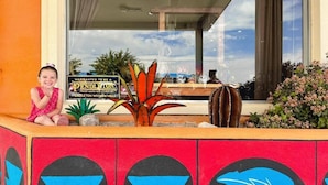 A child sitting in a colorful outdoor seating area with a sign that reads "WARRANTED TO BE A PENDELTON WOOLEN MILLS" and a large window with a view of the sky and buildings. - The Classic Desert Aire Hotel (Alamogordo)