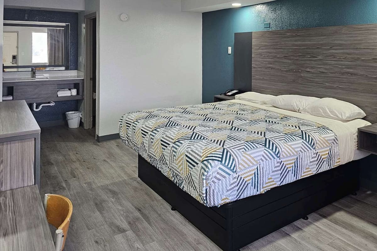 A modern bedroom with a geometric patterned bedspread, a wooden headboard, a bedside table with a lamp, and a built-in nightstand.
