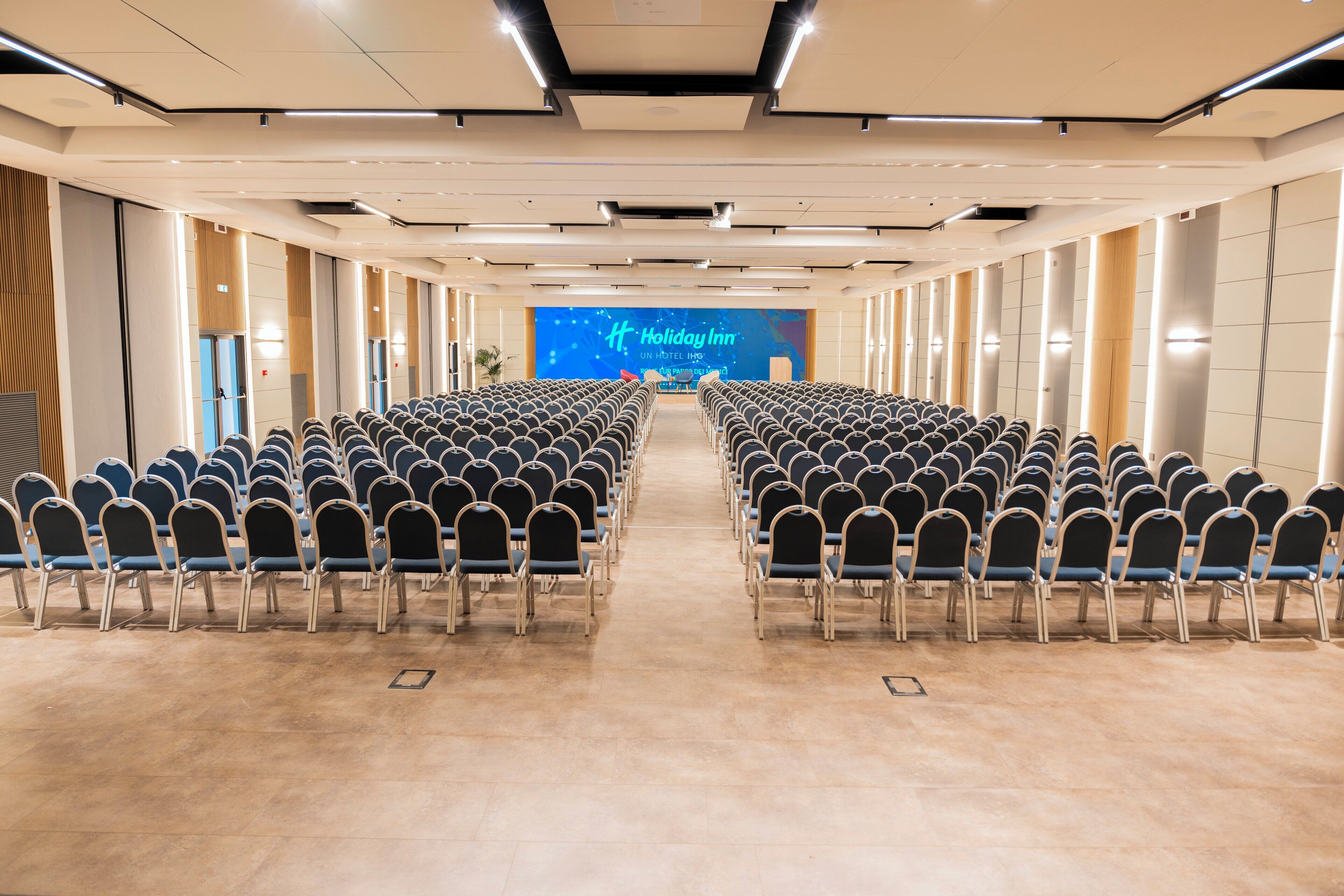 A conference room with rows of chairs facing a large screen displaying 'Holiday Inn' branding.