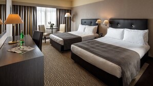 Een hotelkamer met twee bedden, een bureau, een stoel en een raam met gordijnen.