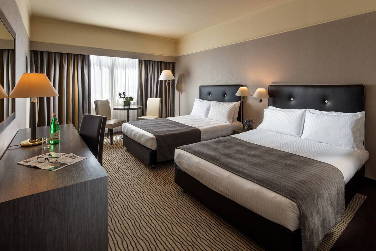 A hotel room with two beds, a desk, a chair, and a window with curtains.