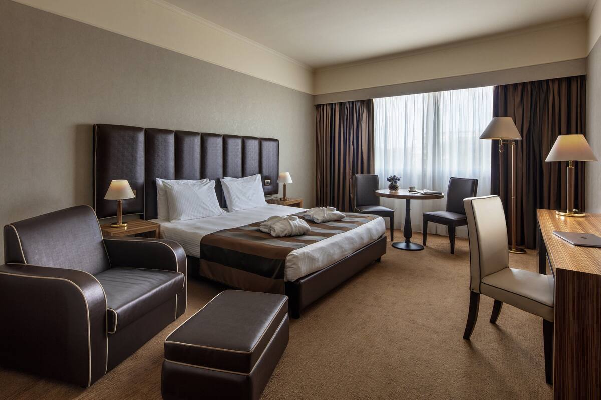 A hotel room with a large bed, a sofa, a desk, and a chair.