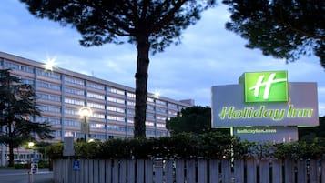 A Holiday Inn sign with a large tree in the foreground.