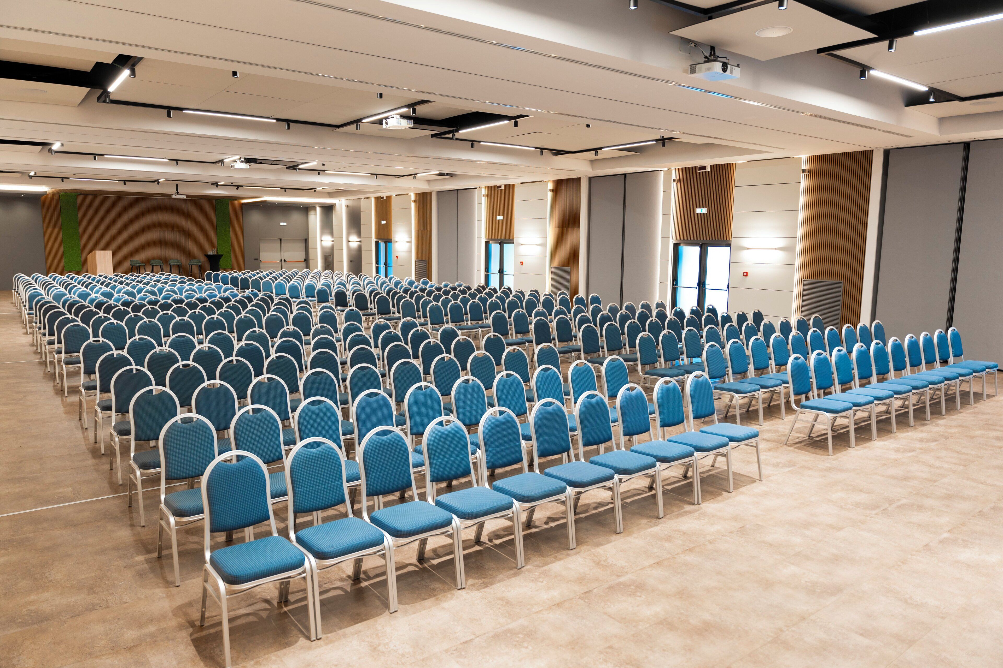 Une salle de conférence avec des rangées de chaises bleues et une estrade.