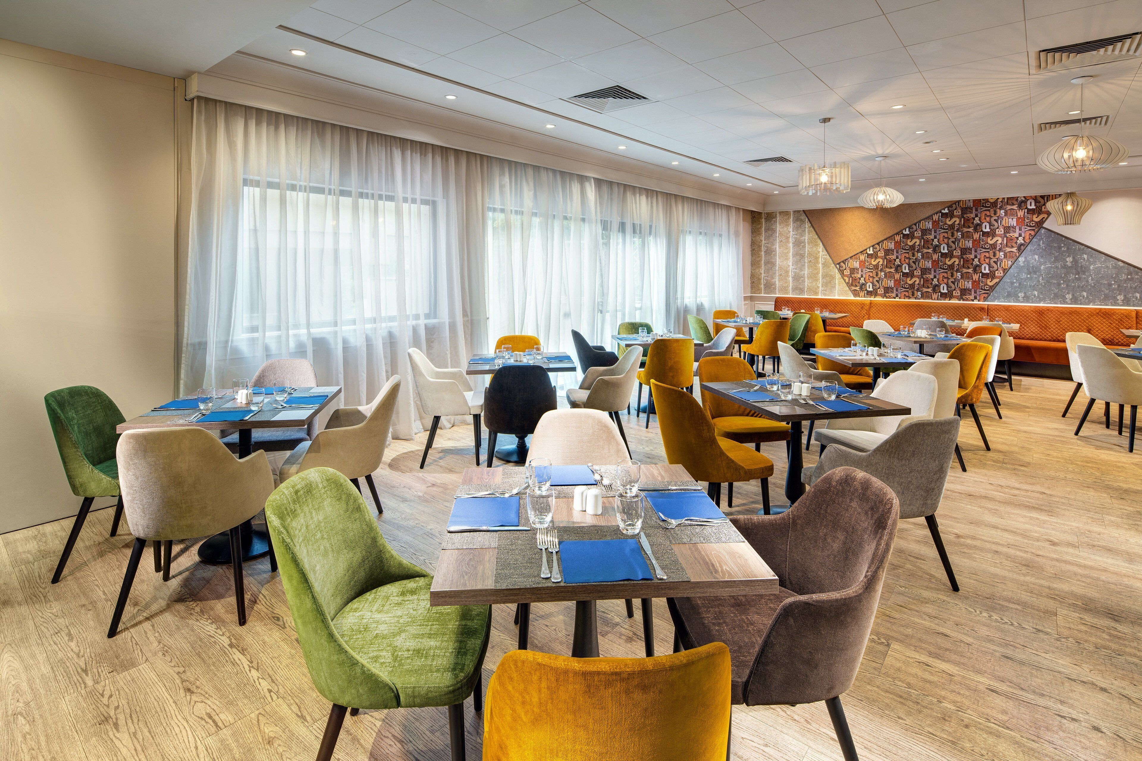 A dining area with multiple tables and chairs, large windows with sheer curtains, and a modern interior design.