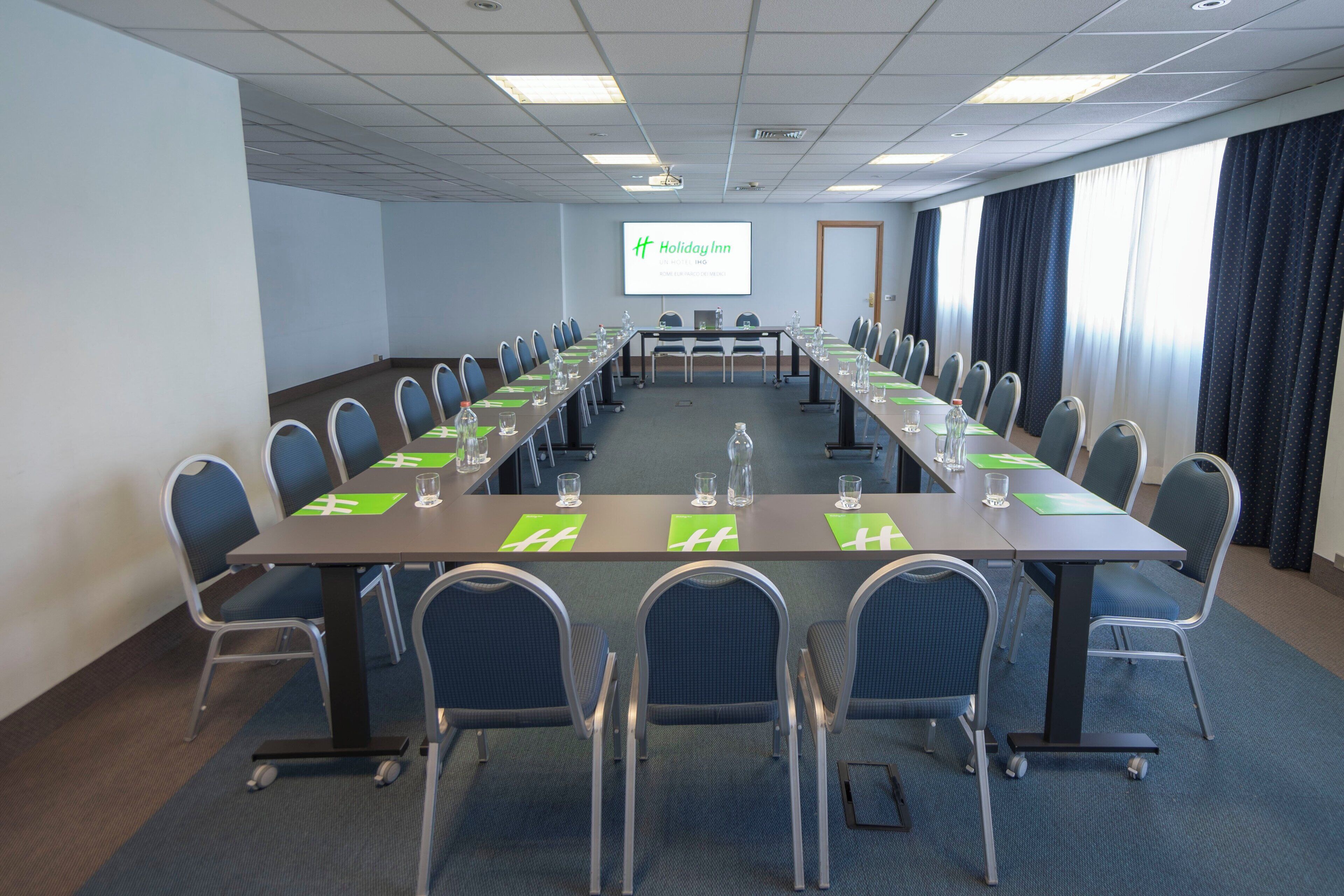 A conference room with a long table, chairs, and a screen displaying 'Holiday Inn' branding.