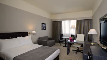 Una habitación de hotel con una cama grande, un escritorio con una silla, un televisor y una ventana con cortinas.