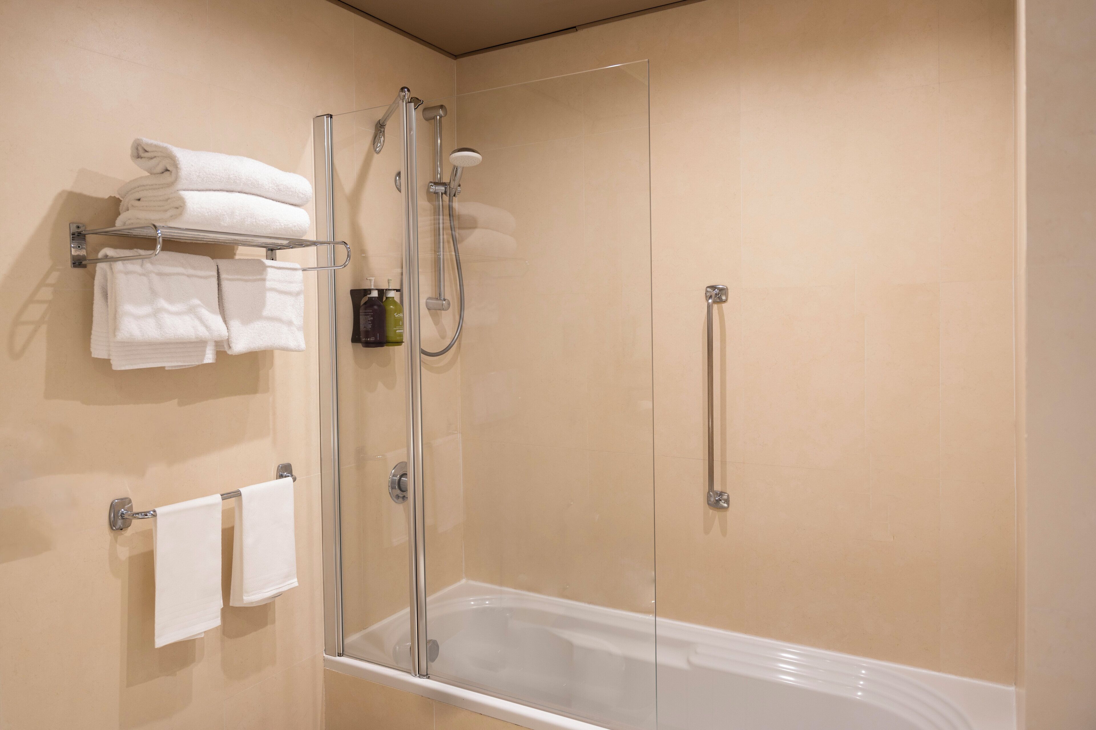 A modern bathroom with a glass-enclosed shower, a white bathtub, and neatly arranged towels on a rack and towel bar.