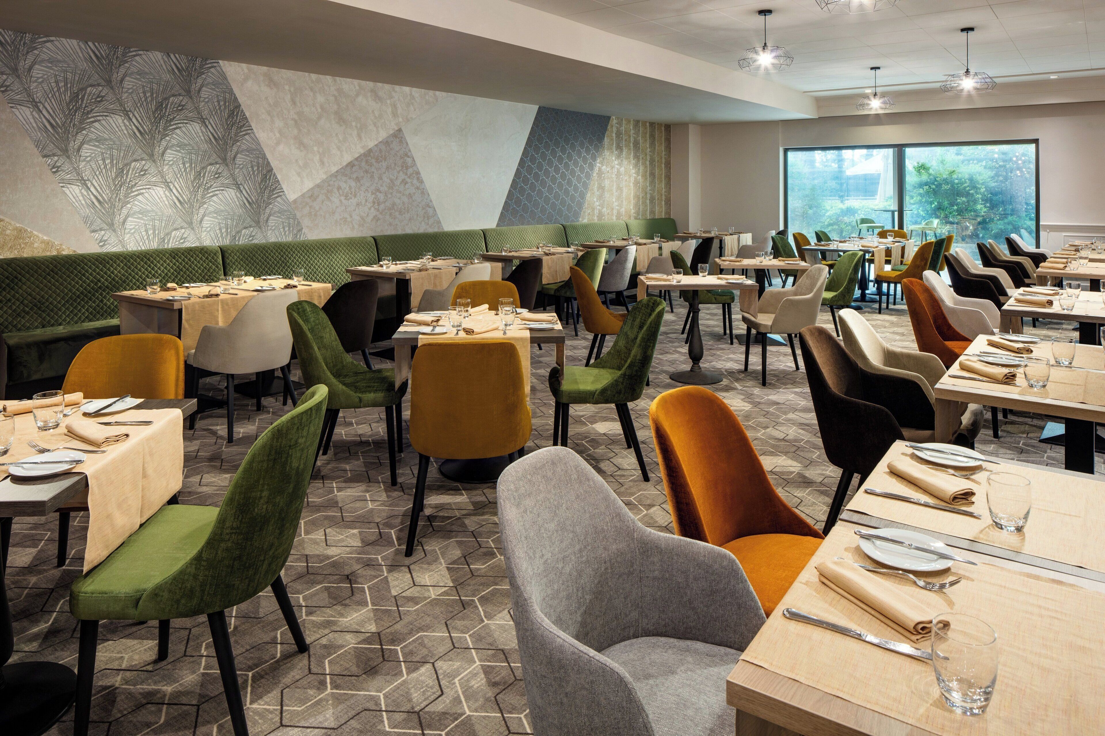 Een restaurant met meerdere tafels en stoelen, een patroonmuur en uitzicht door grote ramen.