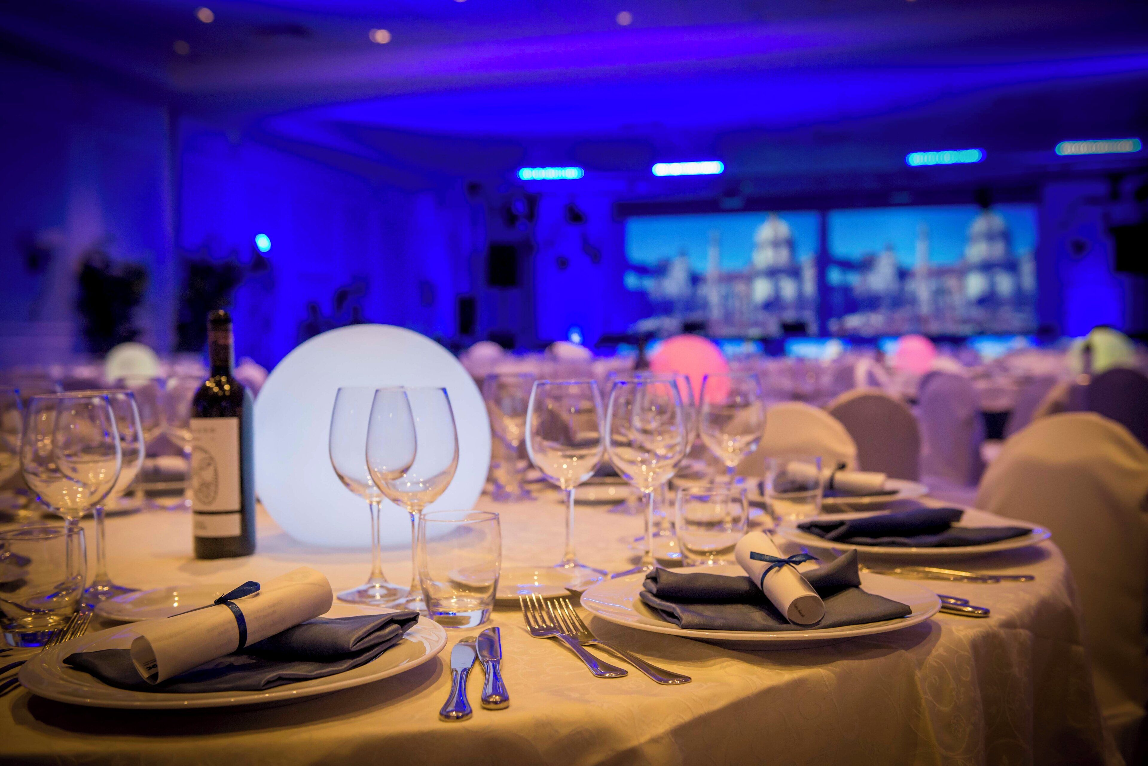 A banquet table set with plates, glasses, cutlery, and a bottle of champagne.