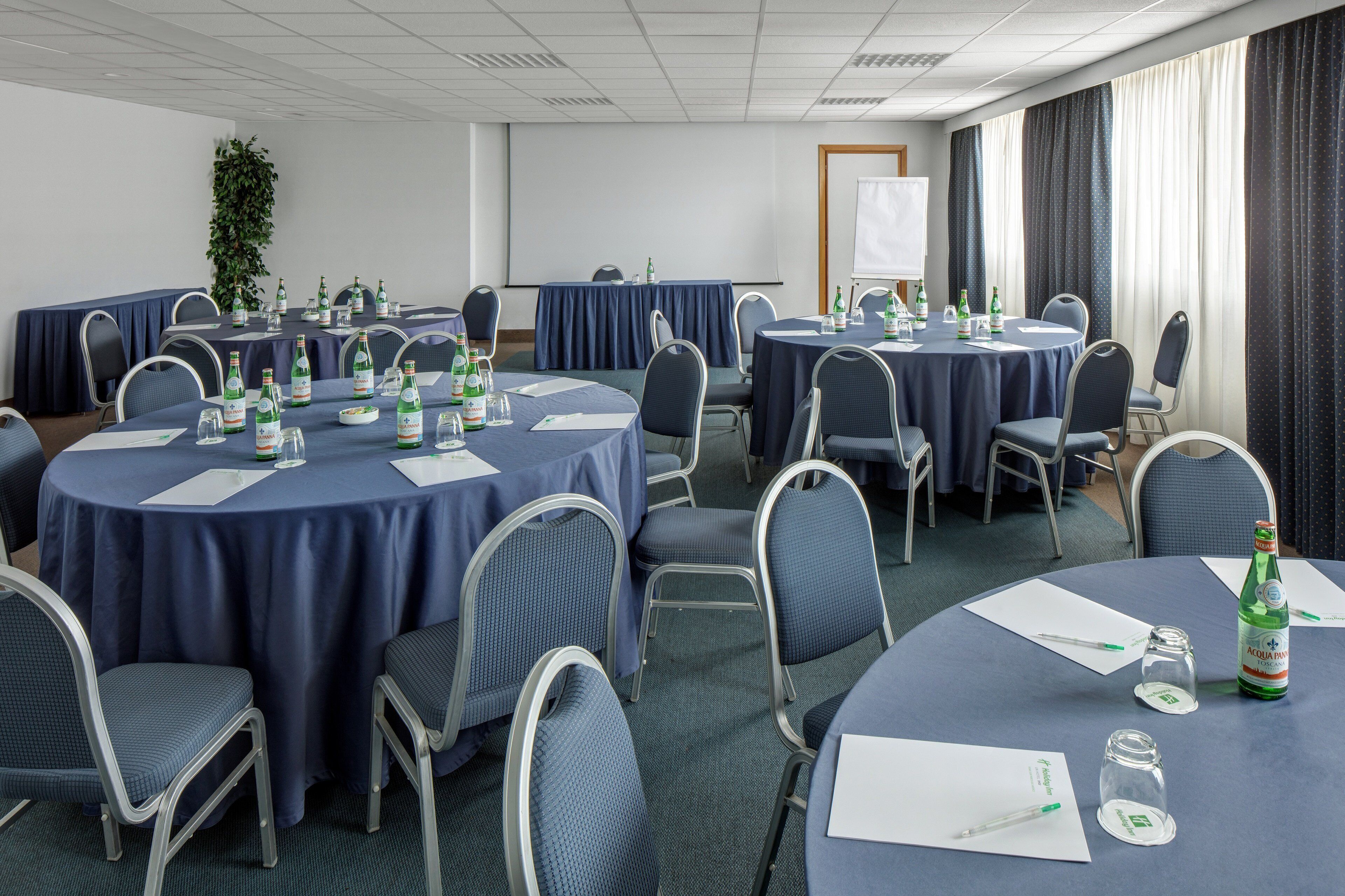 A conference room with round tables, chairs, and a projector screen.