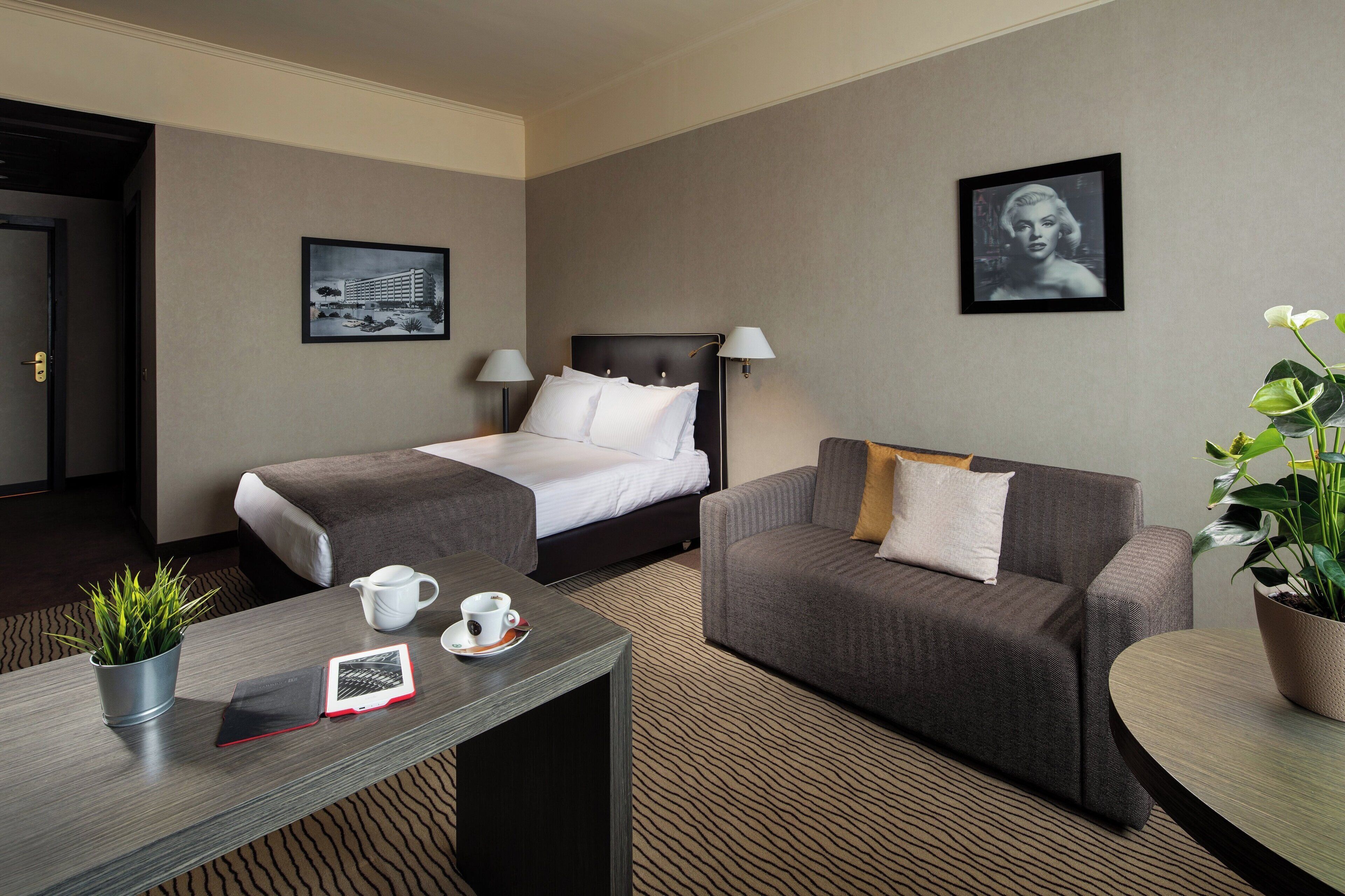 A hotel room with a bed, a sofa, a coffee table, and a plant.