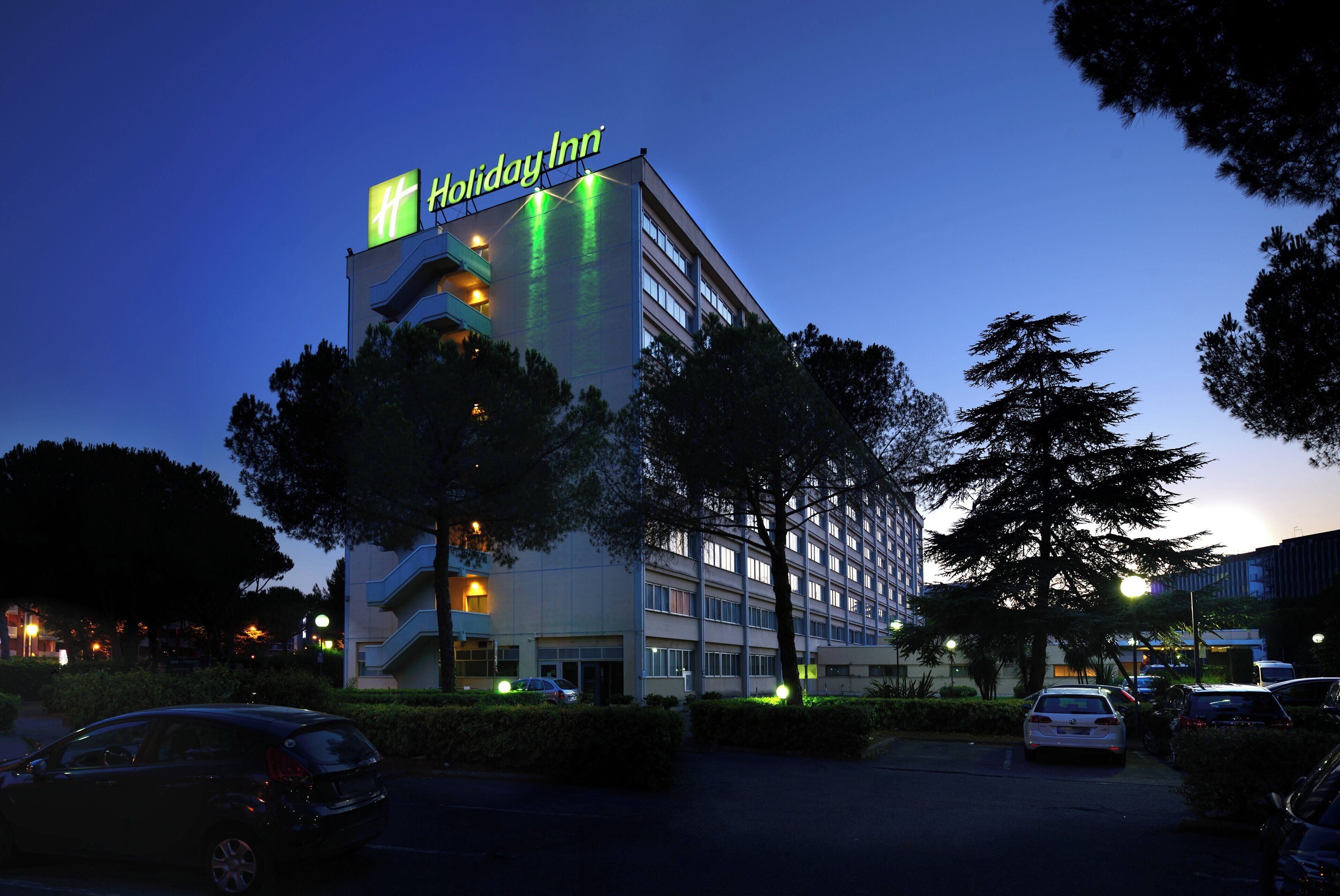 A Holiday Inn hotel with a modern design, multiple floors, and a parking lot with cars.
