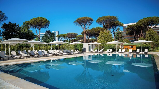 A swimming pool with lounge chairs and umbrellas, surrounded by trees and buildings. - Holiday Inn Rome- Eur Parco Dei Medici by IHG (Rome)