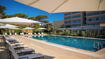 A poolside area with lounge chairs and umbrellas, a clear blue pool, and a modern building in the background.