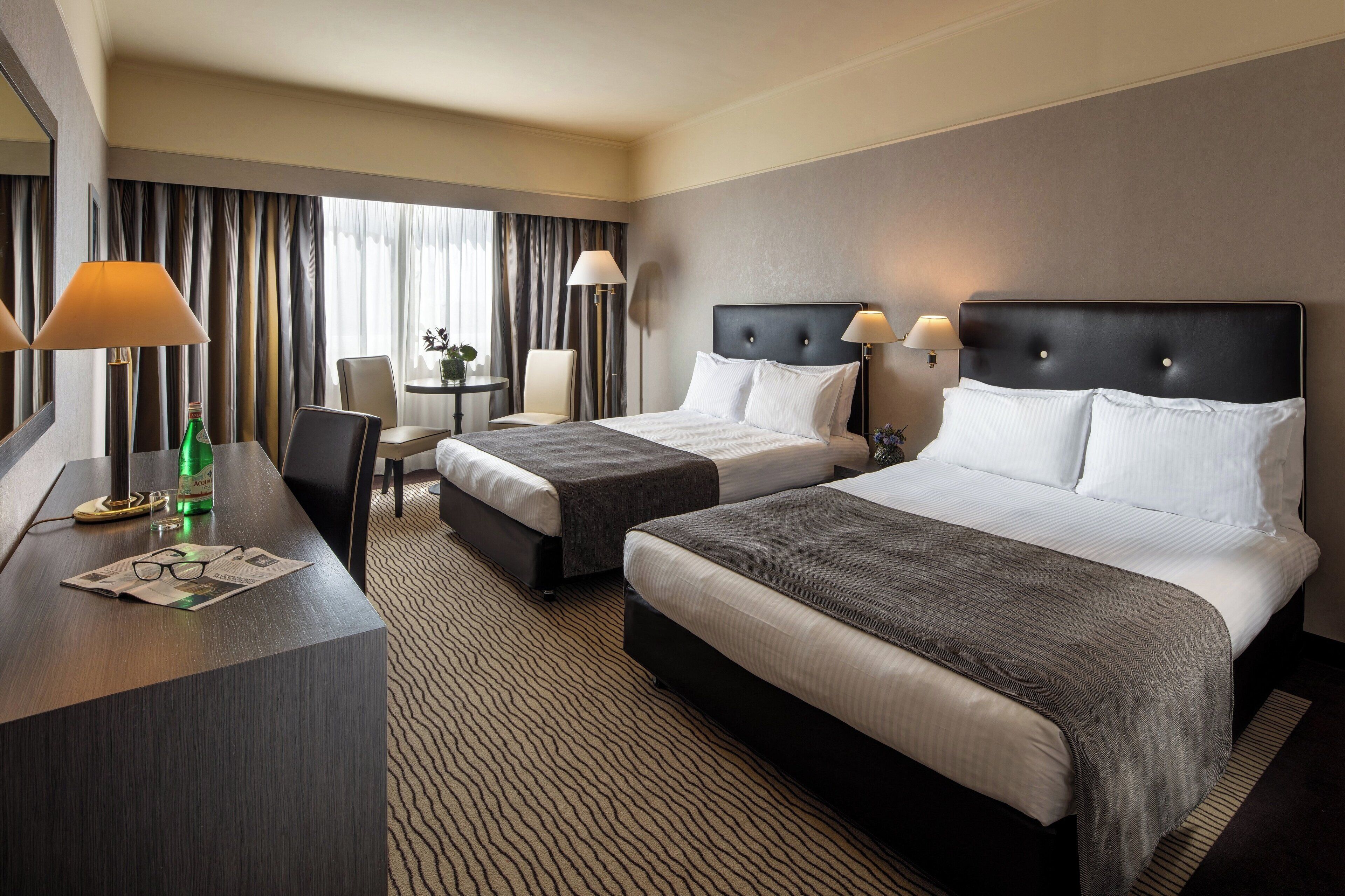 A hotel room with two beds, a desk, and a chair.