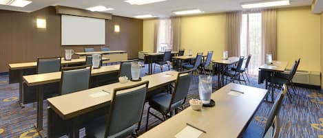 A conference room with multiple tables and chairs, a projector screen, and a large window with curtains.
