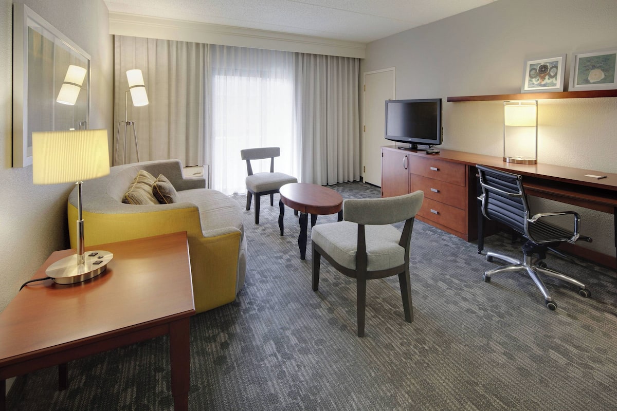 Een hotelkamer met een bank, twee stoelen, een bureau met een computer, een televisie en een lamp.