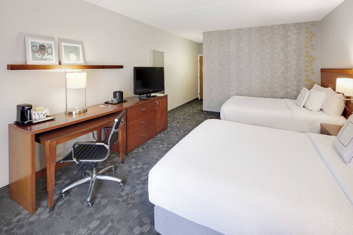 Een hotelkamer met een bed, een bureau met een computer en een stoel, een televisie en een lamp.