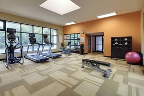 Un gimnasio con cintas de correr, elípticas, una bicicleta estática, una máquina de remo y una pelota de ejercicio roja.